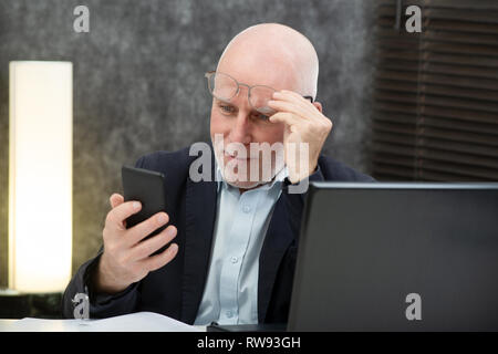Un imprenditore senior utilizzando lo smartphone, egli sta avendo difficoltà e problemi di visione Foto Stock