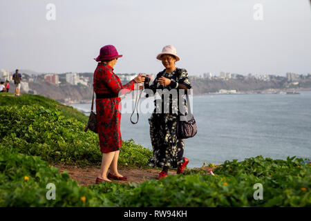 Lima, Perù - Febbraio 22 2019: turisti asiatici di scattare le foto del tramonto al Malecón de la Costa Verde, donna passando la fotocamera ad un amico Foto Stock