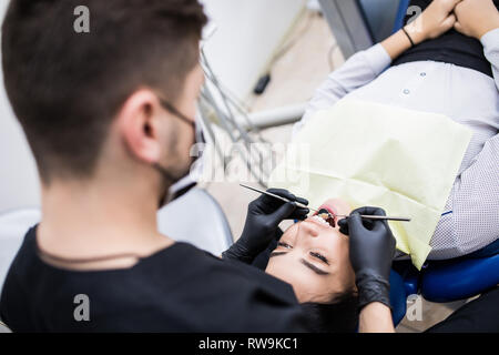 Dentista esamina i denti del paziente sulla poltrona del dentista Foto Stock