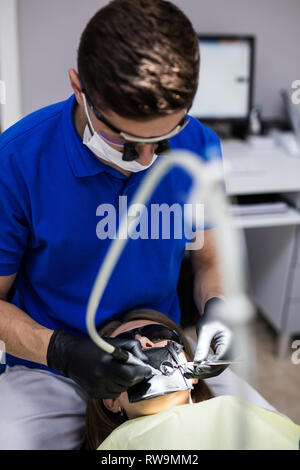 Uomo al dentista clinica riceve il trattamento dentale per riempire una cavità di un dente. Restauro dentale e materiale composito trattare di polimerizzazione di denti. Foto Stock