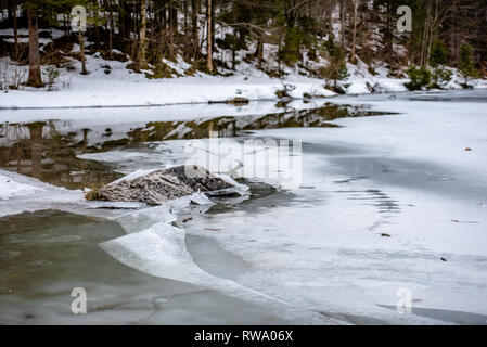 Uno spesso strato di ghiaccio sul lago ghiacciato a Vorderer Langbathsee. Belle montagne dalle vette innevate riflessa nelle acque cristalline del lago Foto Stock