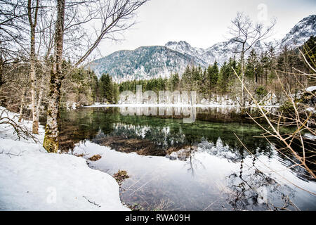Uno spesso strato di ghiaccio sul lago ghiacciato a Vorderer Langbathsee. Belle montagne dalle vette innevate riflessa nelle acque cristalline del lago Foto Stock