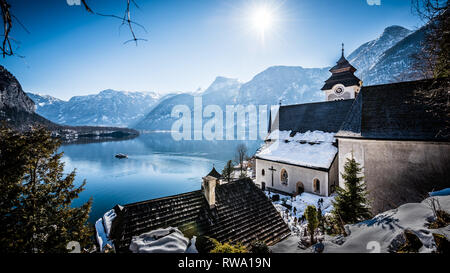La Chiesa cattolica si affaccia sul bellissimo lago di Hallstattersee circondato da montagne dalle vette innevate Foto Stock