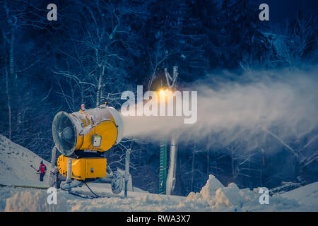 Snow making machine sulla collina produrre neve sulla pista da sci in inverno sera Foto Stock