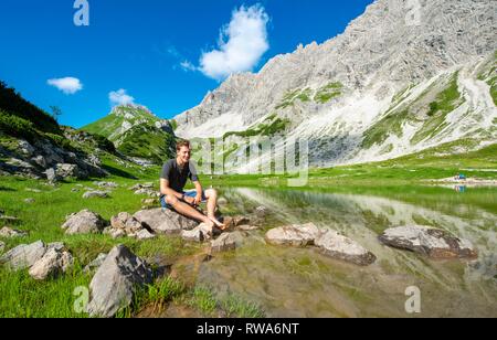 Giovane uomo si siede sulla pietra, lago di montagna a Prinz-Luitpold-Haus, Algovia Alpi, Bad Hindelang, Algovia, Baviera, Germania Foto Stock