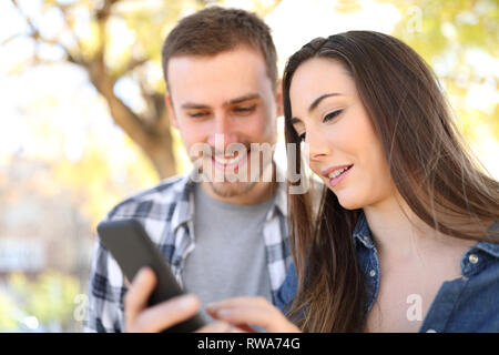 Felice coppia utilizzando smart phone controllando il contenuto online di un parco Foto Stock