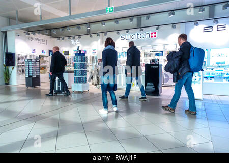 I passeggeri sulla strada per l'aereo passano intorno alle offerte di molti marchi famosi in tutto il mondo, aeroporto a piedi Swatch, aeroporto di Vienna, Austria Foto Stock