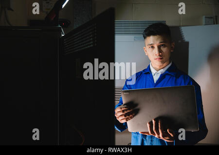 Giovane uomo è guardando la telecamera mentre nella stanza del server con un computer portatile. Foto Stock