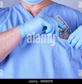 Medico maschio mette un batuffolo di dollari nella sua tasca della camicia, concetto di prendere tangenti ai servizi medici Foto Stock