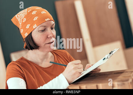 Falegname femmina iscritto DIY note del progetto dopo la finitura gabbia in legno per la sua piccola attività laboratorio di falegnameria Foto Stock