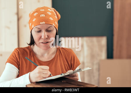 Falegname femmina iscritto DIY note del progetto dopo la finitura gabbia in legno per la sua piccola attività laboratorio di falegnameria Foto Stock