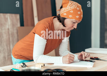 Falegname femmina con il fazzoletto di testa facendo il calcolo finanziario in falegnameria officina di falegnameria Foto Stock