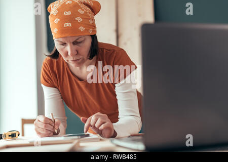 Falegname femmina con il fazzoletto di testa facendo il calcolo finanziario in falegnameria officina di falegnameria Foto Stock