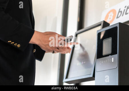 Imprenditore acquisto e trasferimento cryptocurrency per telefono cellulare dal bancomat per le operazioni di acquisto e di vendita cryptocurrency. Foto Stock
