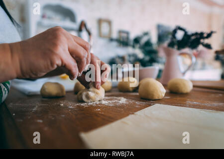 Le mani di una donna in cucina formatura di impasti palle. La formazione di palline di pasta per la cottura sul tavolo di legno. Foto Stock