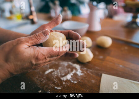 Le mani di una donna in cucina formatura di impasti palle. La formazione di palline di pasta per la cottura sul tavolo di legno. Foto Stock