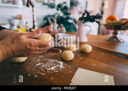 Le mani di una donna in cucina formatura di impasti palle. La formazione di palline di pasta per la cottura sul tavolo di legno. Foto Stock