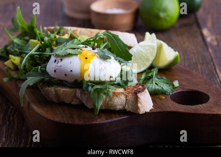 Sandwich vegetariano con uovo in camicia, avocado, rucola su fette di pane tostato e sana colazione o uno spuntino rustico di legno, fuoco selettivo, chiudi Foto Stock