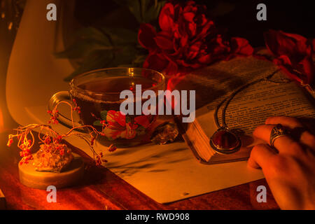 Ancora una vita. Tazza di tè su un tavolo. Peonia su un tavolo. La lettura del libro. Un uomo di sfogliare le pagine del libro interessante. Decorazione di gioielli Foto Stock