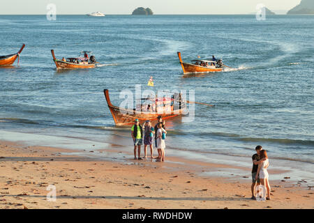 Lunga coda di barche per island hopping, Aonang, Krabi, Thailandia, turisti che lasciano le barche nel surf, sera sun Foto Stock