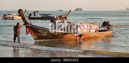 Lunga coda di barche per island hopping, Aonang, Krabi, Thailandia, turisti che lasciano le barche nel surf, sera sun Foto Stock
