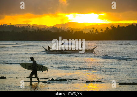Surfer con tavola da surf, passeggiate sulla spiaggia con tour in barca e il sole di setting di distanza - Cloud 9 - Siargao, Filippine Foto Stock