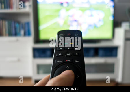 Mano che tiene un controllo remoto nella parte anteriore dello schermo del televisore Foto Stock