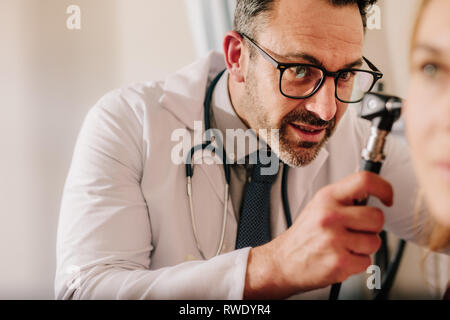 Esperto medico ORL cercando in orecchio del paziente con un otoscopio. Medico maschio esaminando orecchio del paziente con strumento a sua clinica. Foto Stock