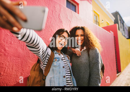 Bella giovane donna rendendo selfie con il suo migliore amico all'esterno. Eccitati viaggiatori femmina tenendo selfie con lo smartphone. Foto Stock