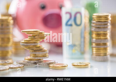 Rosa salvadanaio in medio dei rotoli di banconote in euro e torri con le monete Foto Stock
