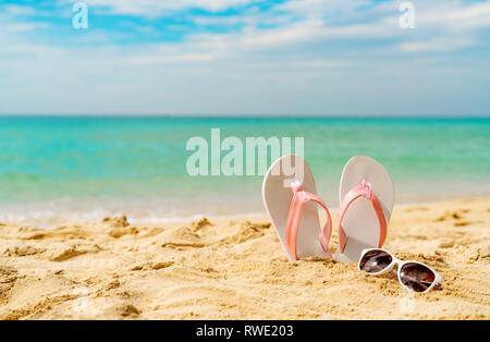 Rosa e Bianco sandali, occhiali da sole sulla spiaggia di sabbia in riva al mare a. Moda casual style flipflop e bicchieri. La vacanza estiva sulla spiaggia tropicale. Vacanza divertente Foto Stock
