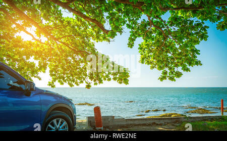 Blue sport Auto SUV parcheggiata dal mare tropicale sotto ombrellone albero. La vacanza estiva in spiaggia. Estate viaggi in automobile. Viaggio su strada. Industria automobilistica. Foto Stock