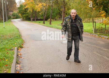 Il lettone uomo a camminare lungo la strada suburbana, Skrunda, Lettonia Foto Stock