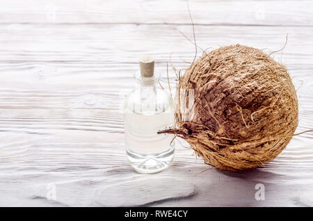 Le noci di cocco e olio in un barattolo di vetro bianco su un tavolo di legno. Il concetto di cura Foto Stock