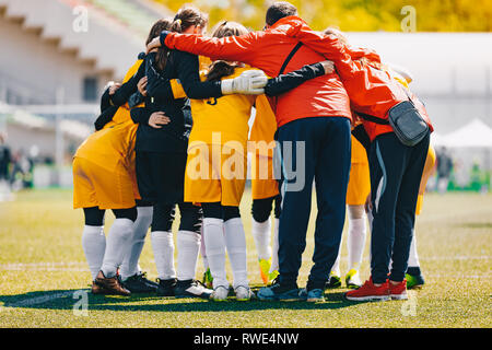 Coaching Coach ragazze team sportivo. Ragazze scuola di sport team huddling con pulmann sul campo in erba. Calcio ragazze junior team a sport outdoor Foto Stock