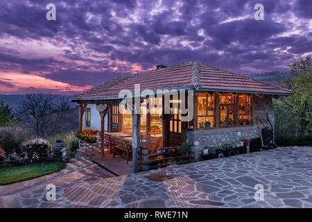 Bella tradizionale serbo Ethno house al tramonto con soffici nuvole blu del cielo e le luci all'interno della casa Foto Stock