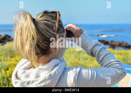 Giovane donna guardando attraverso il binocolo al mare in estate. La balena o bird watching Foto Stock