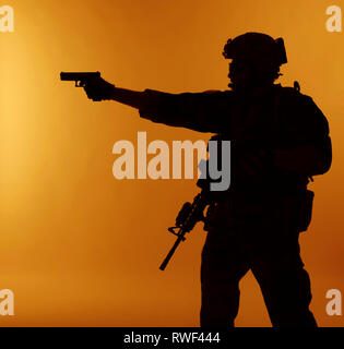 Silhouette di U.S. Marine Corps Marsoc raider puntando pistola, sfondo arancione. Foto Stock