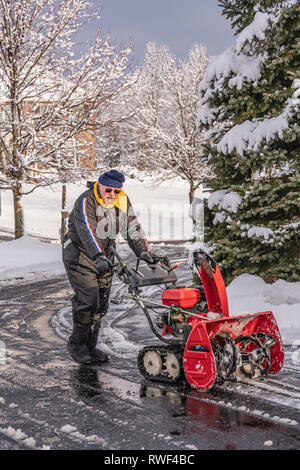 Senior Citizen con lo spalaneve dopo aver cancellato il vialetto di neve da una tempesta di neve Foto Stock