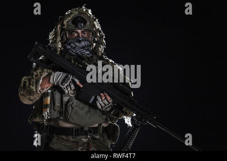 Army Sniper con faccia dipinta, tenendo un grande fucile. Foto Stock