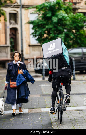 Parigi, Francia - Sep 12, 2017: vista posteriore del ciclista Deliveroo fast ciclismo su strada francese a fornire alimenti con vicino a donne in cammino noleggio Consegna del cibo Foto Stock