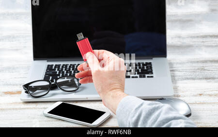 Stretta di mano maschio holding thumb drive USB con tecnologia workstation in background per affari o per l'uso scolastico Foto Stock