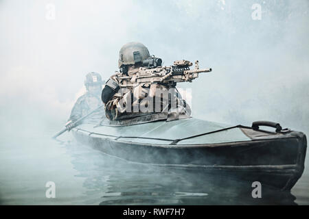 Le forze speciali operatore armato di mitragliatrice, Esercito di canoa kayak attraverso la nebbia di fiume. Foto Stock