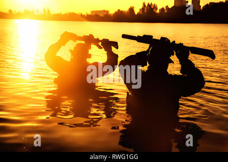 Le forze speciali militari con fucili a canna rigata sopra la testa prima di attraversare un fiume durante una giungla raid. Foto Stock