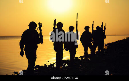 Silhouette di esercito di soldati con fucili contro un tramonto arancione. Foto Stock