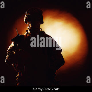 Silhouette di esercito di soldato in uniforme di combattimento con fiery spot su sfondo nero. Foto Stock