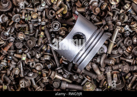 Piatto di metallo laici un nuovo pistone dalla vettura si trova sullo sfondo di un gran numero di dispositivi di fissaggio: dadi, viti, viti di diverse dimensioni, vista dall'alto. Il Foto Stock