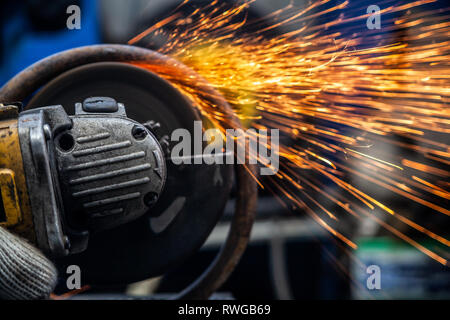 Close-up di un uomo di segatura di metallo del cuscinetto con una mano la sega circolare, luminoso lampeggia battenti in direzioni diverse in background gli strumenti per un auto Foto Stock