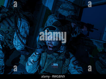 Commando team leader urlando in radio ricevitore durante un corso intensivo di firefight di notte. Foto Stock