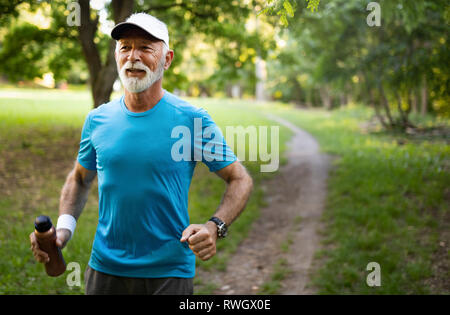 Pensione attraente uomo con un bel sorriso a fare jogging nel parco Foto Stock